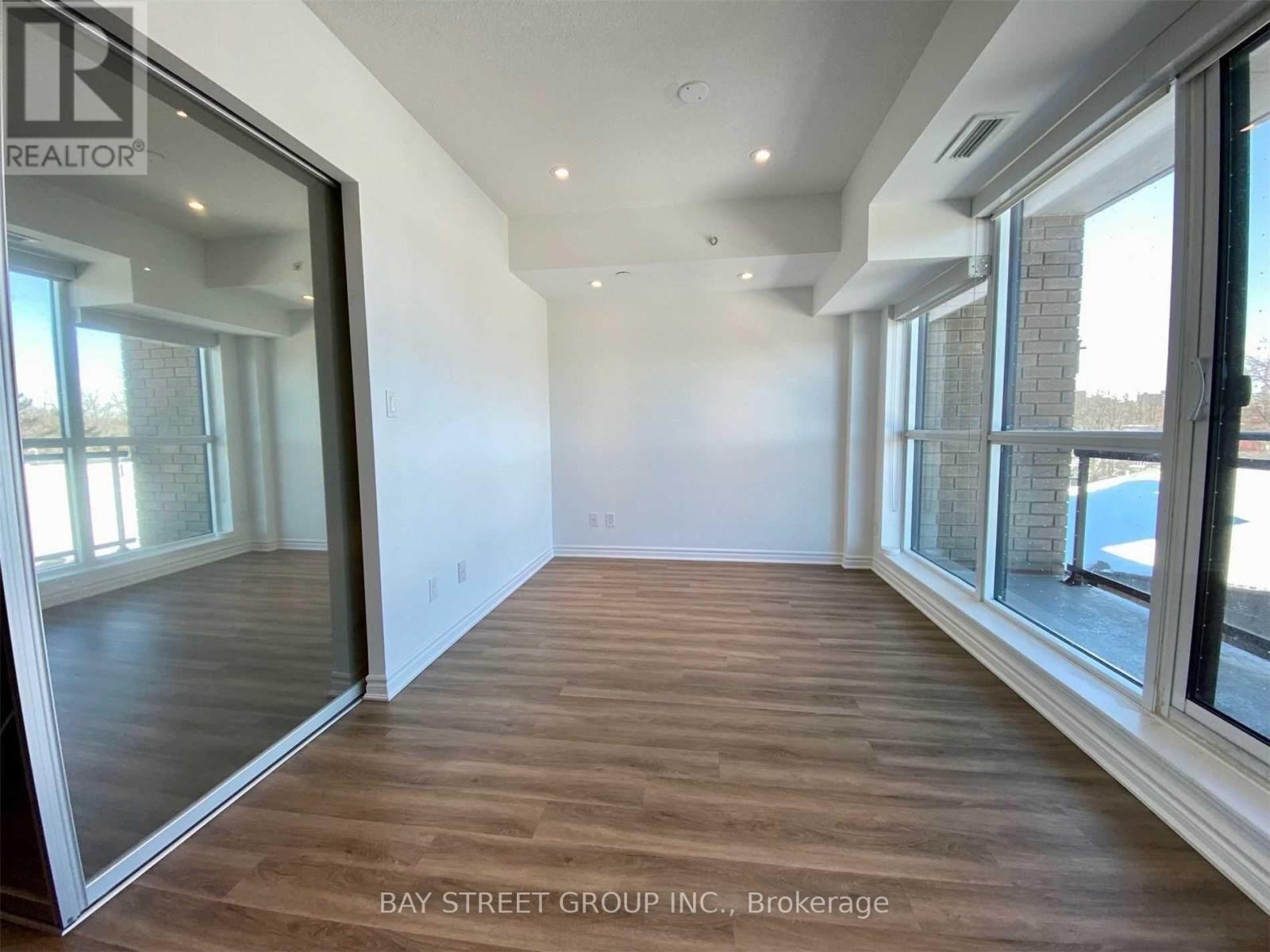A spacious room with wooden flooring and large windows.