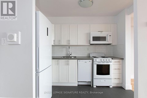 A white kitchen with a refrigerator, microwave, oven and sink.