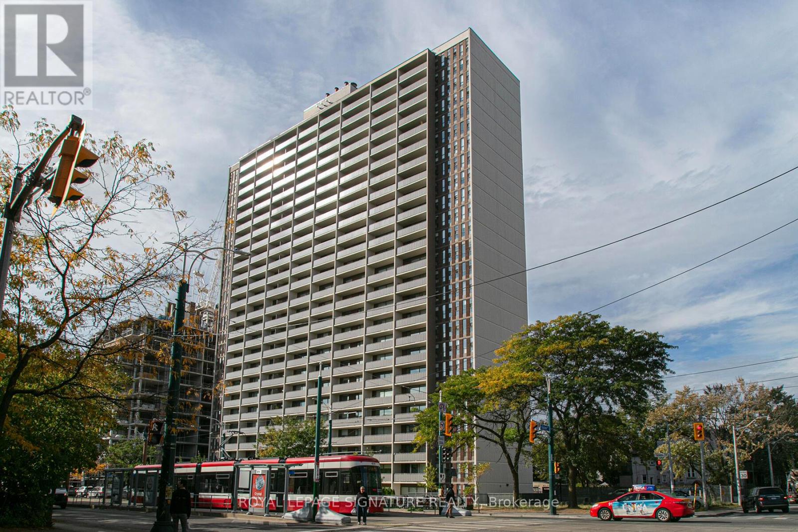 A tall building with a glass facade stands in front of a tree with autumn leaves.