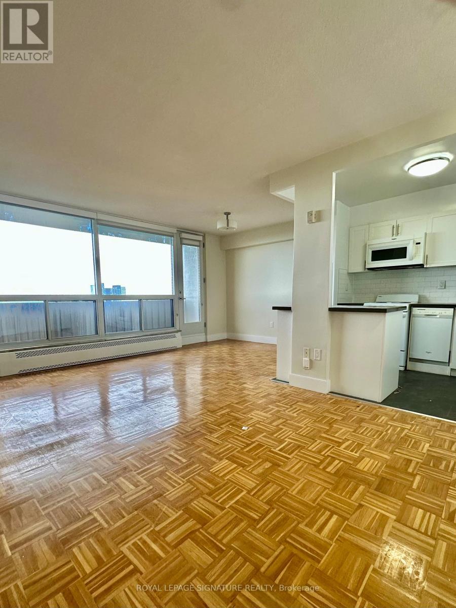 A room with wooden flooring and a kitchen area in the background.