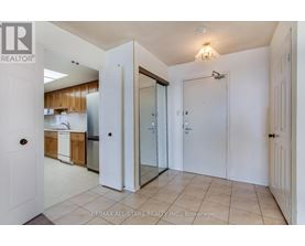 A white door opens to a kitchen with wooden cabinets and a stainless steel refrigerator.