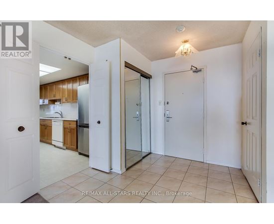 A white door opens to a kitchen with wooden cabinets and a stainless steel refrigerator.