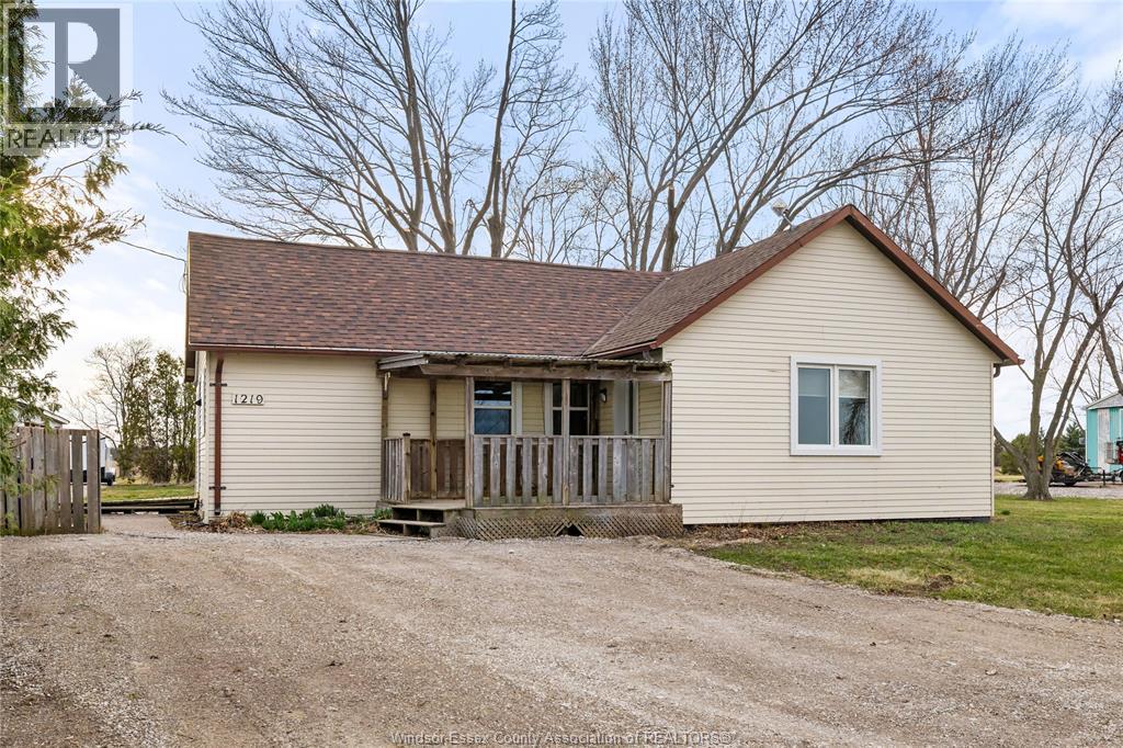 A small house with a porch and a brown roof is surrounded by a gravel driveway.