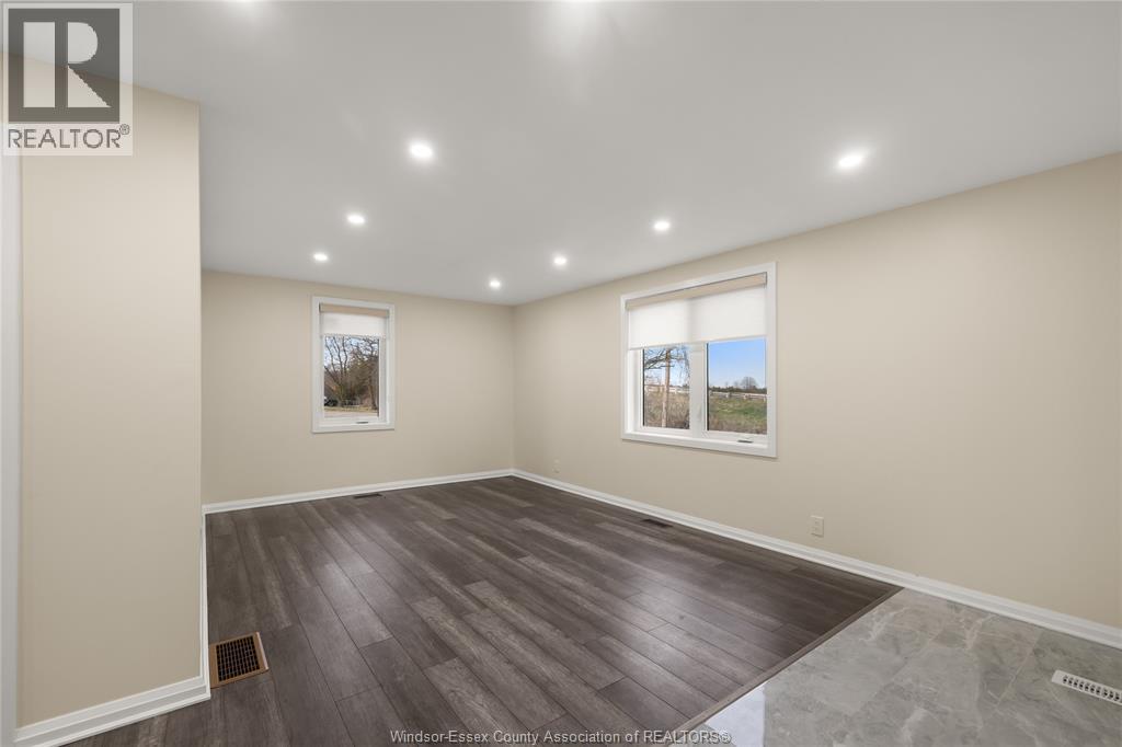 A spacious room with wooden flooring and two windows.