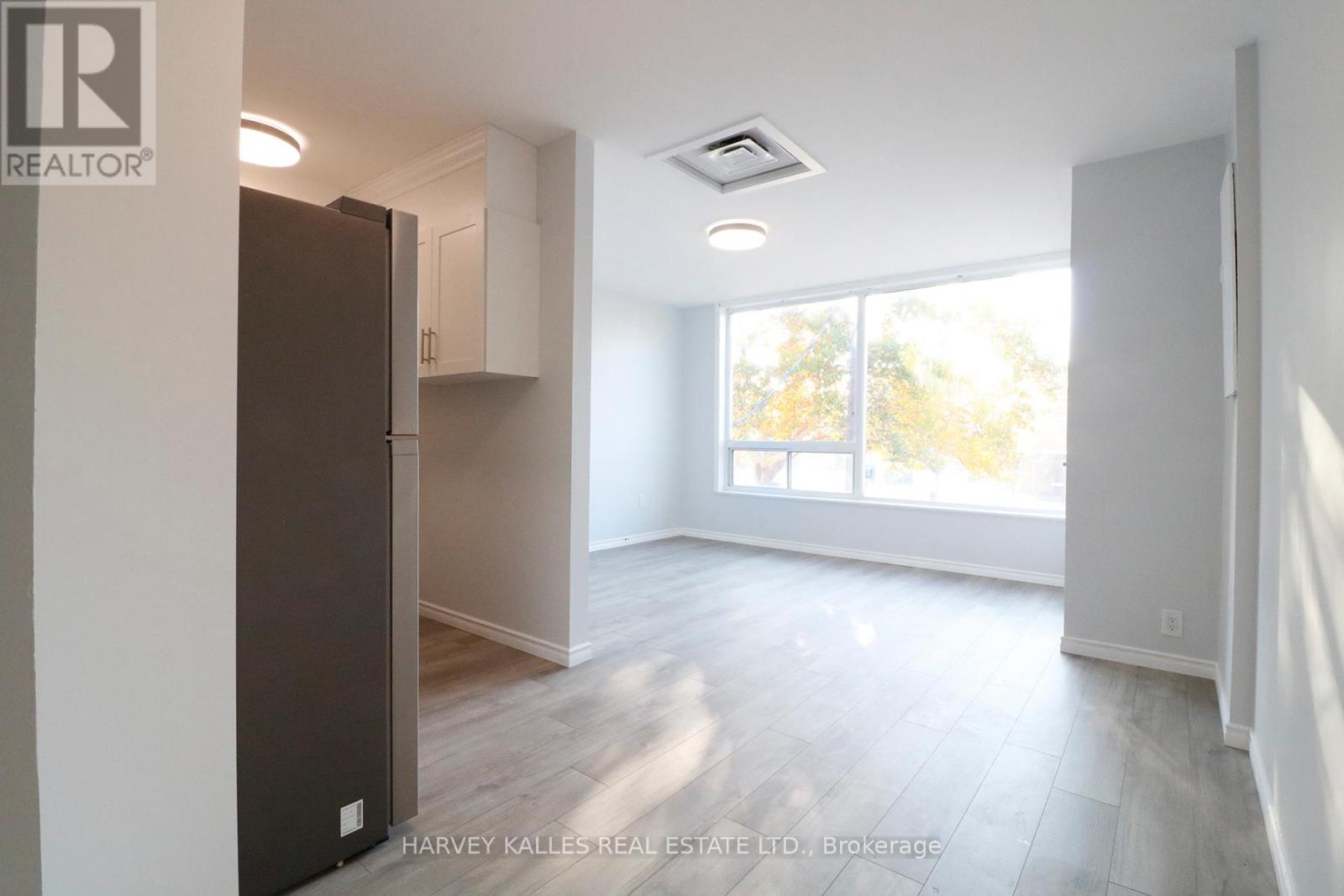 A spacious, empty room with a large window and a refrigerator.