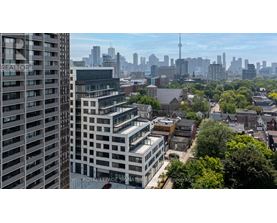 A cityscape with a mix of modern and older buildings, with the CN Tower visible in the distance.