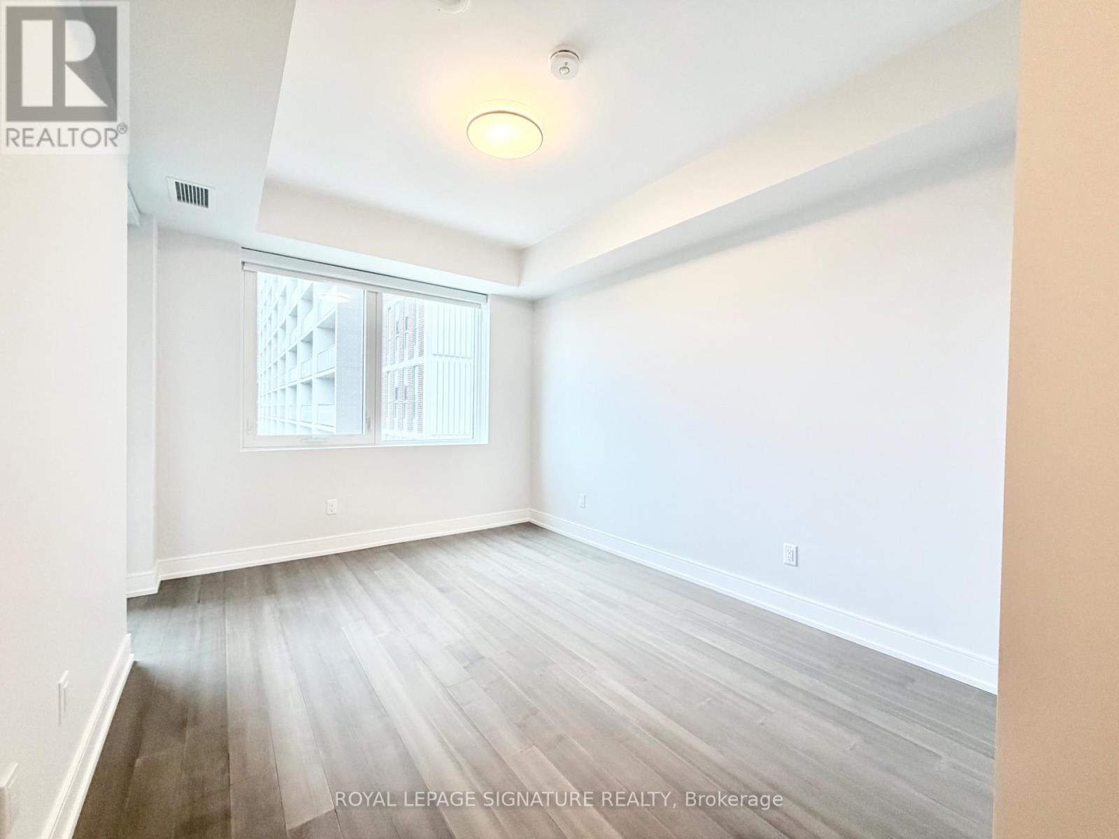 A room with white walls and wooden flooring, with a window showing a building outside.