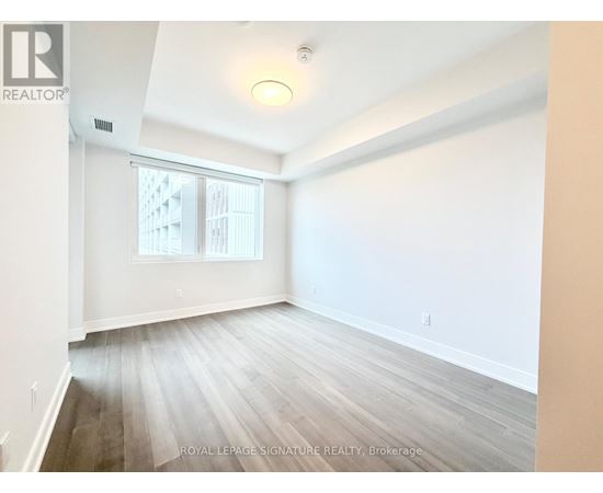 A room with white walls and wooden flooring, with a window showing a building outside.
