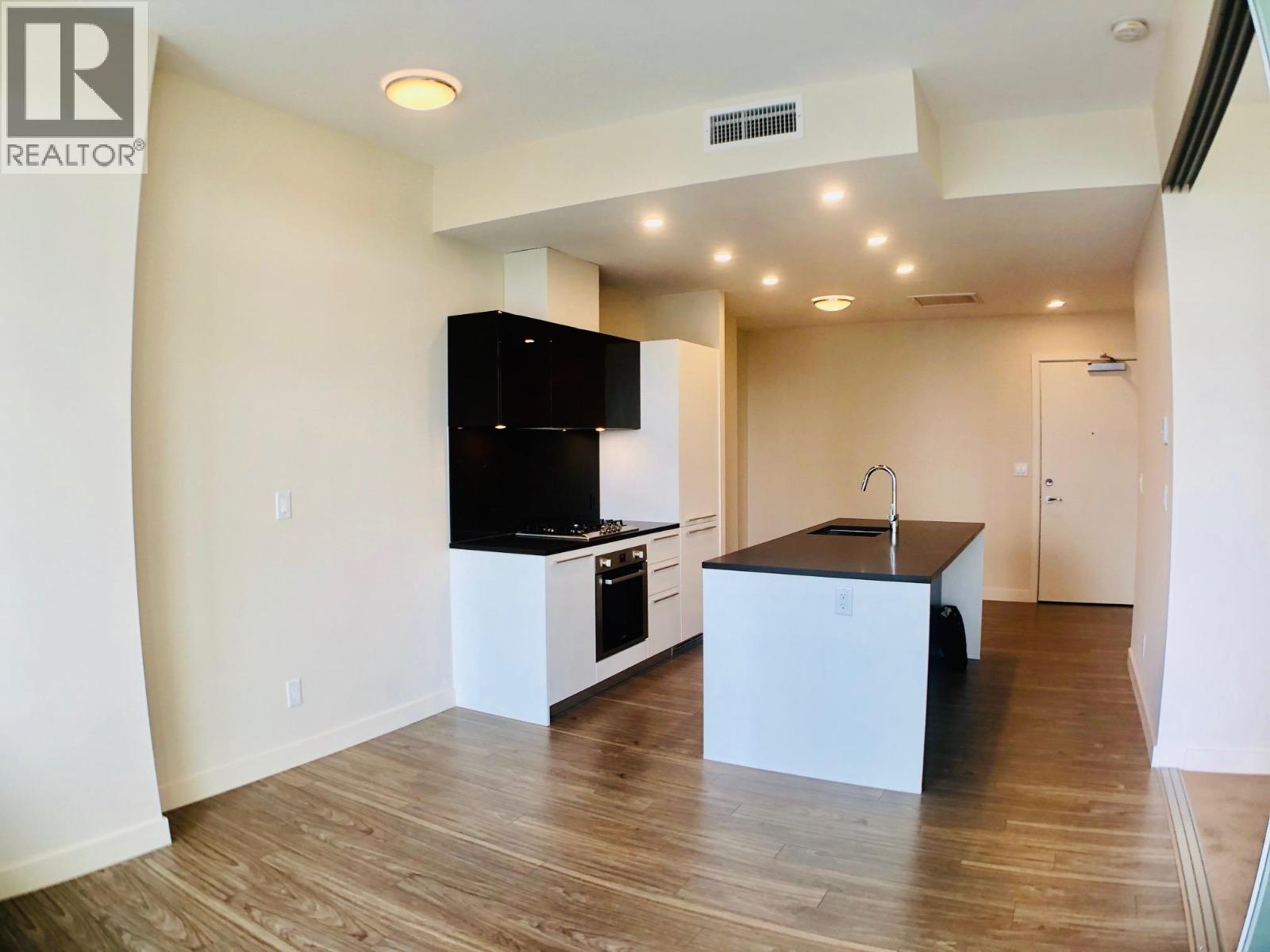 A modern kitchen with wooden floors and a black countertop.