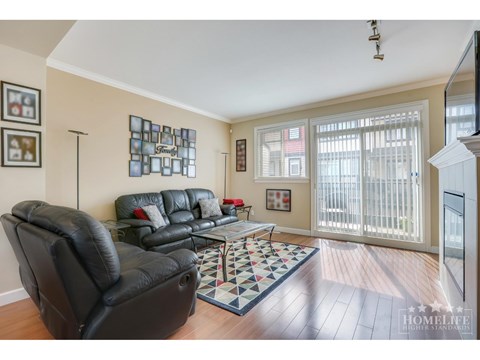 A living room with a black leather couch and a checkered rug.