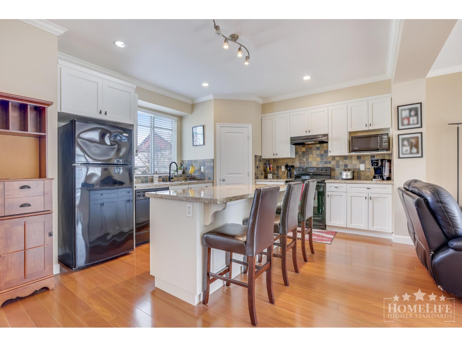 A kitchen with a black fridge and wooden chairs.