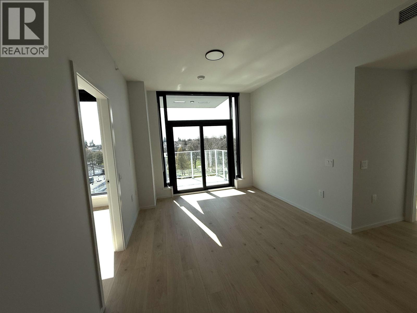 A spacious room with wooden floors and a large window with a view of the outside.