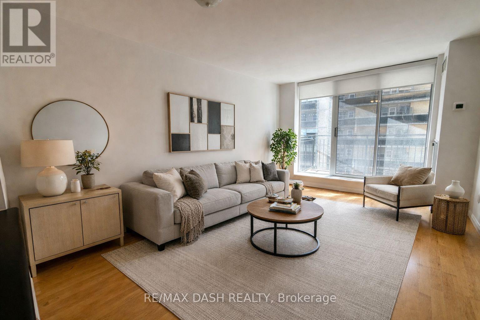 A well-lit living room with a grey sofa, a coffee table, and a large window.