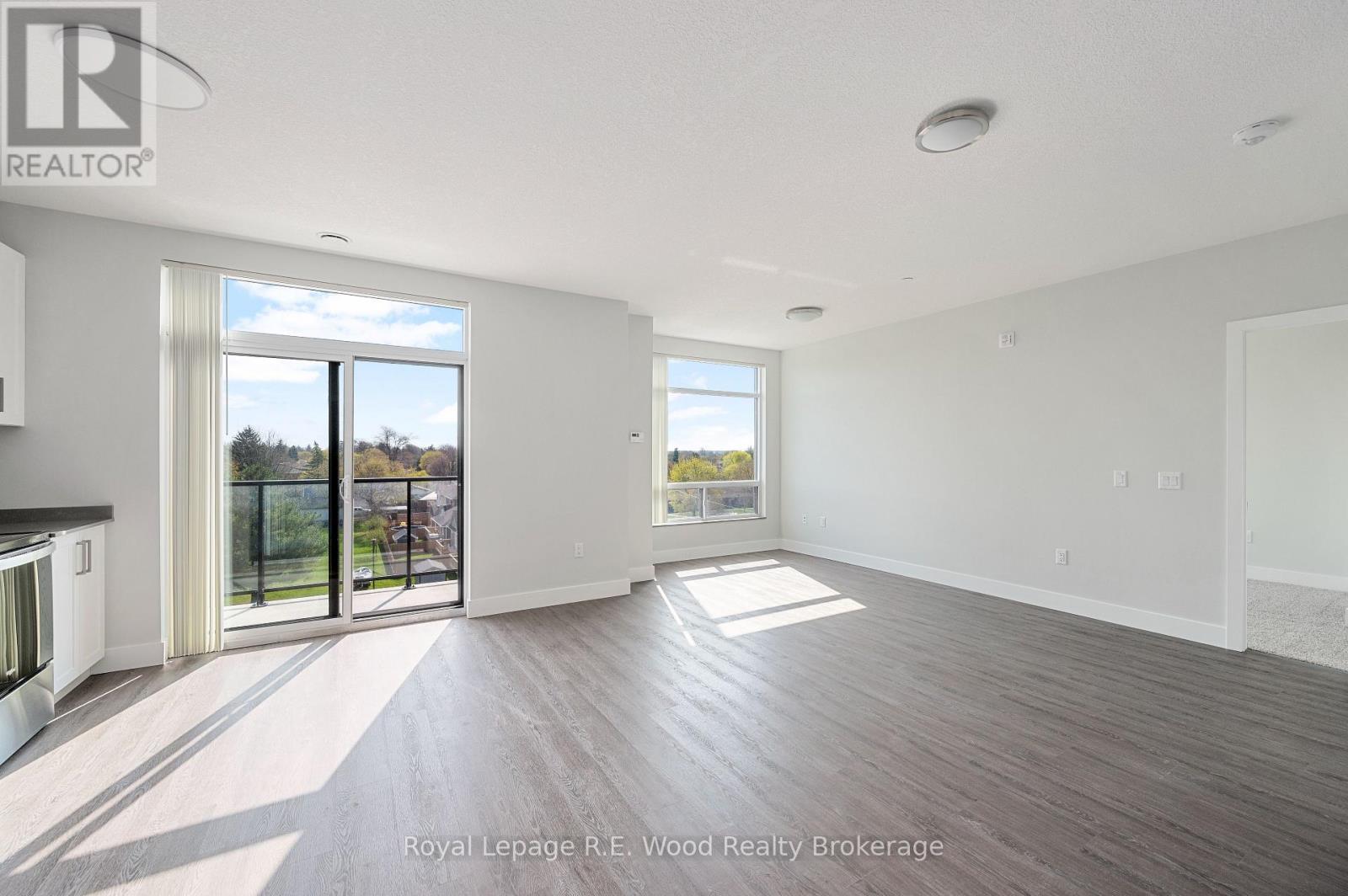 A spacious room with wooden flooring and a large window overlooking a balcony.