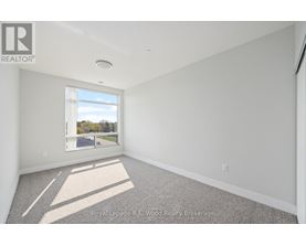 A well lit empty room with a window and carpet on the floor.