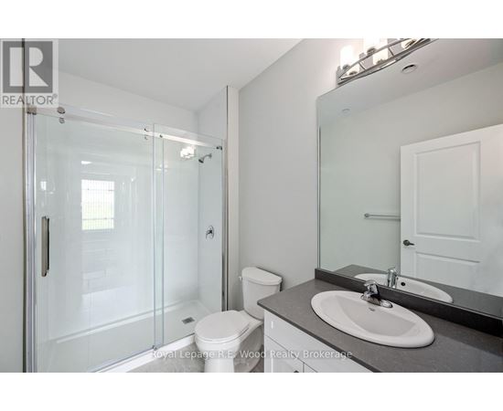 A white toilet sits in a bathroom next to a sink and a walk-in shower.