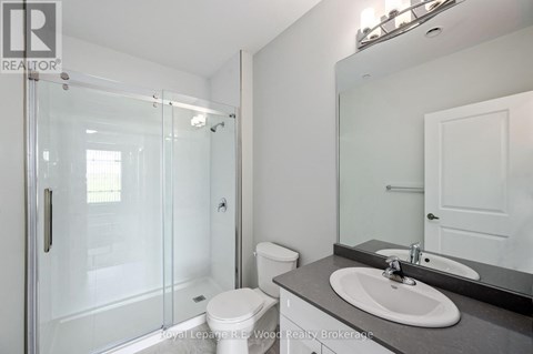 A white toilet sits in a bathroom next to a sink and a walk-in shower.