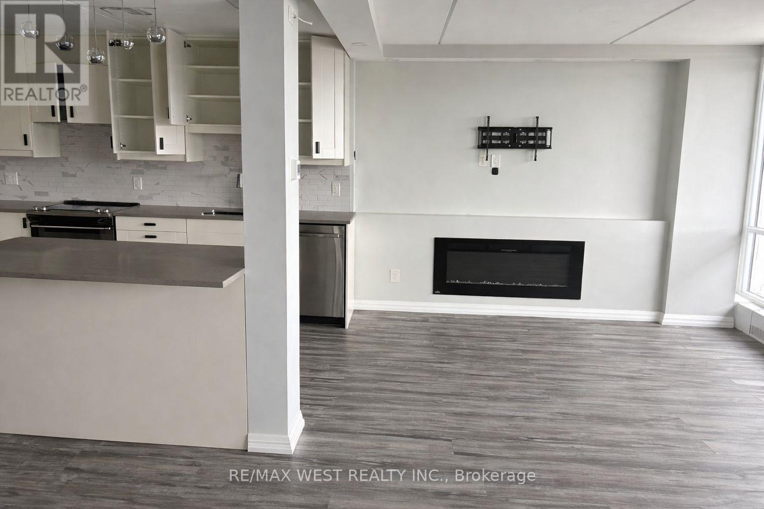 A large, empty room with a fireplace and a kitchen area.