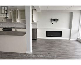 A large, empty room with a fireplace and a kitchen area.
