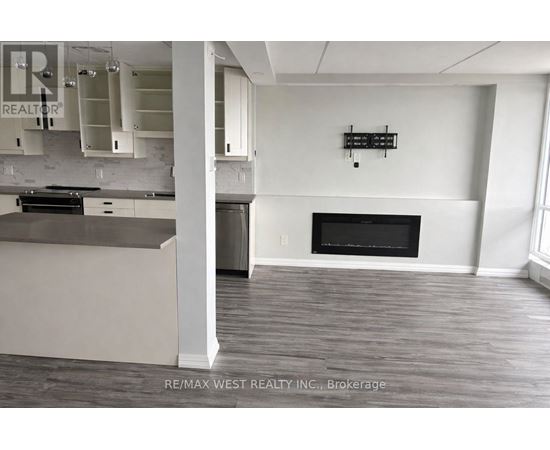 A large, empty room with a fireplace and a kitchen area.