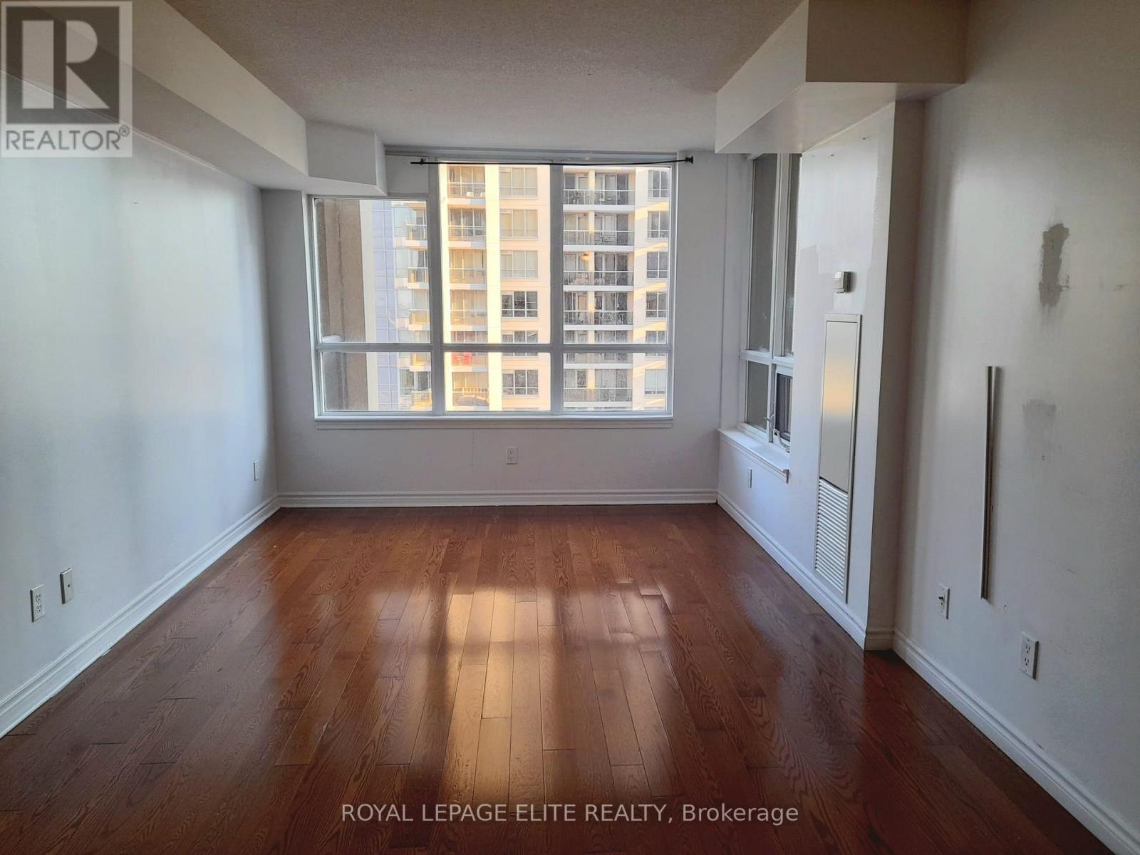 A room with wooden floors and a large window overlooking a building.
