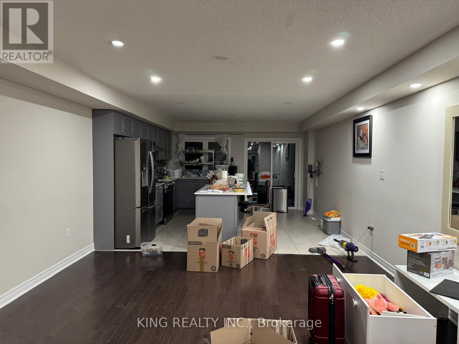 A room with boxes on the floor and a kitchen in the background.