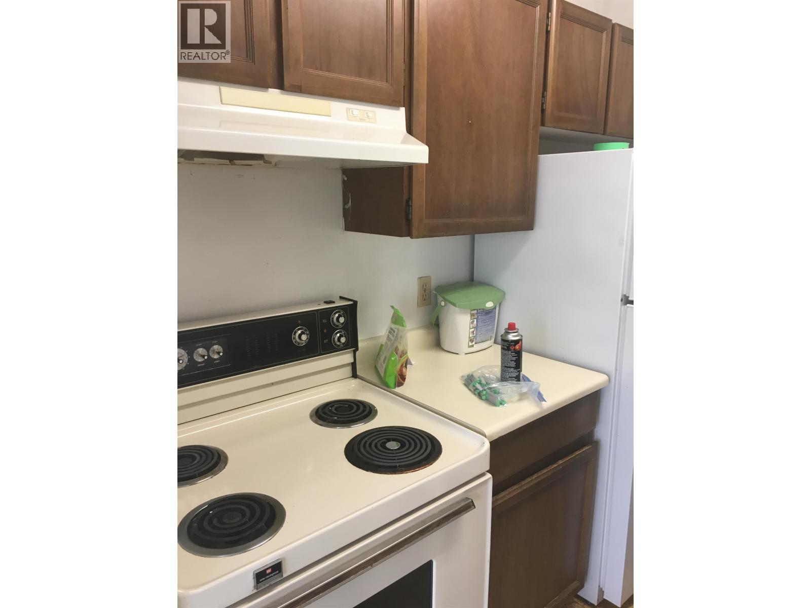 A white stove top oven with four burners and a white refrigerator in a kitchen.