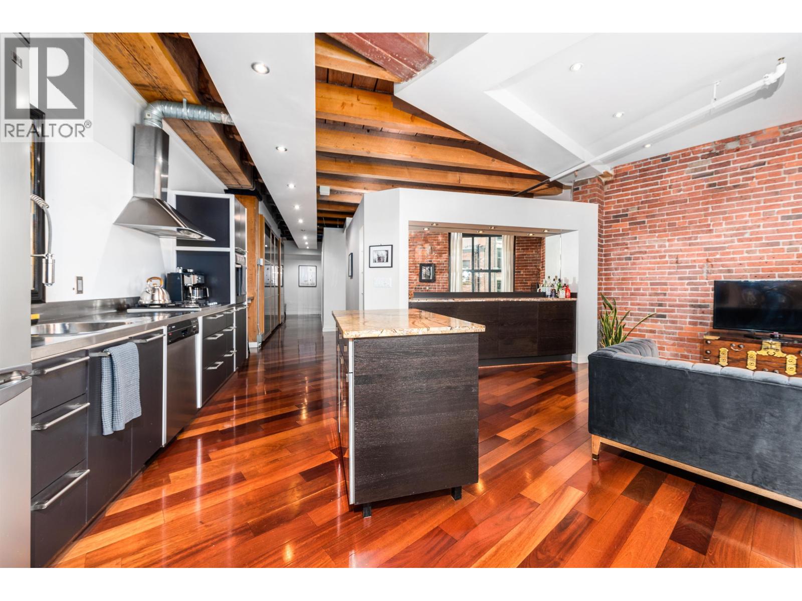 A modern kitchen with wooden floors and a brick wall.