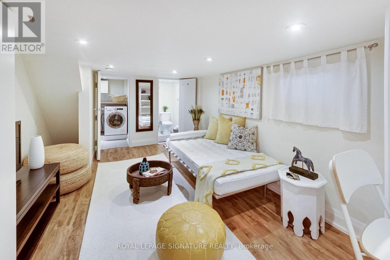 A well-lit, modern bedroom with a bed, chair, and a washing machine in the background.