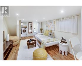 A well-lit, modern bedroom with a bed, chair, and a washing machine in the background.