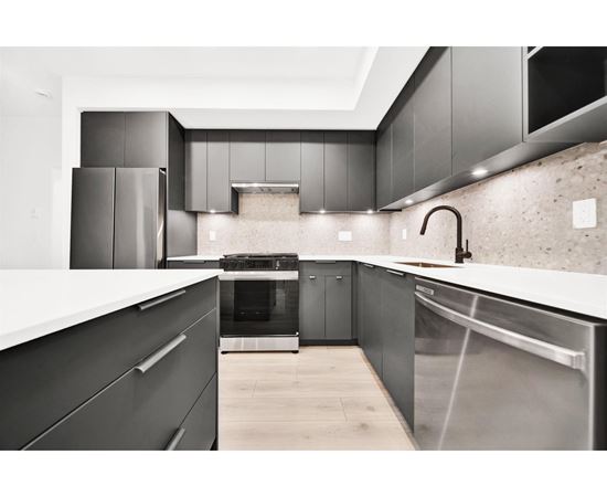 A modern kitchen with dark cabinets and stainless steel appliances.