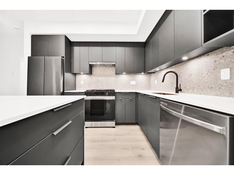A modern kitchen with dark cabinets and stainless steel appliances.