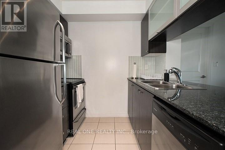 A kitchen with a stainless steel refrigerator and black countertops.