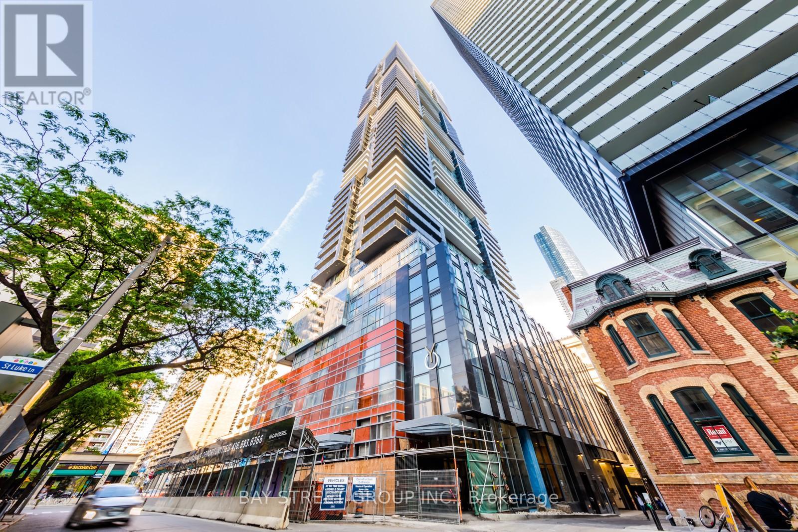A tall building with a glass facade stands in front of a brick building with scaffolding around it.