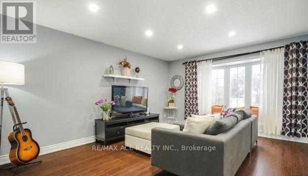 A living room with a grey couch, a guitar, a TV, and a flower vase on a table.