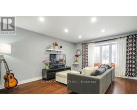 A living room with a grey couch, a guitar, a TV, and a flower vase on a table.