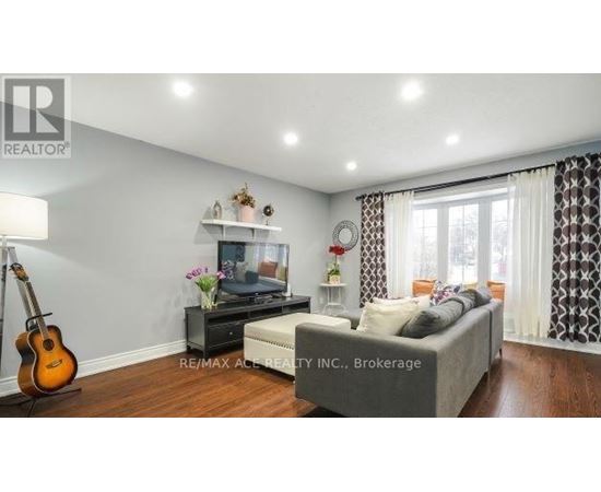 A living room with a grey couch, a guitar, a TV, and a flower vase on a table.