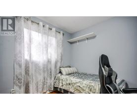 A bedroom with a bed, chair, and window with curtains.