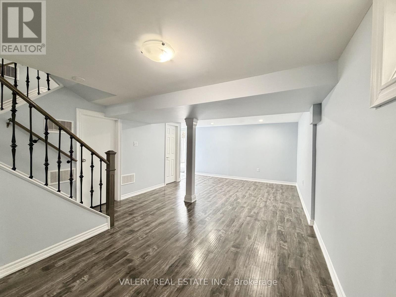 A spacious room with wood flooring and a staircase with a railing.