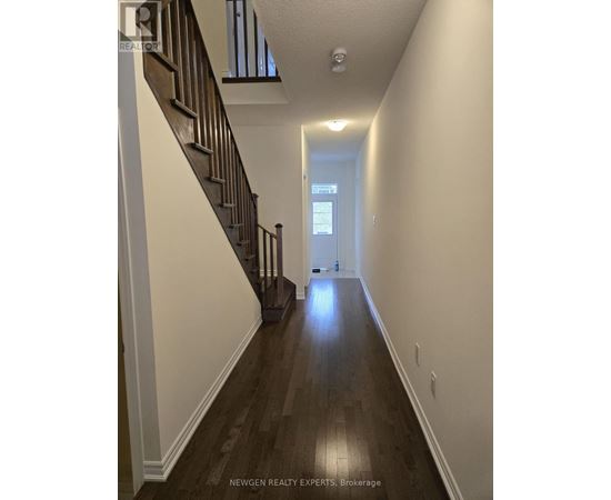 A long hallway with a staircase on the left and a door at the end.