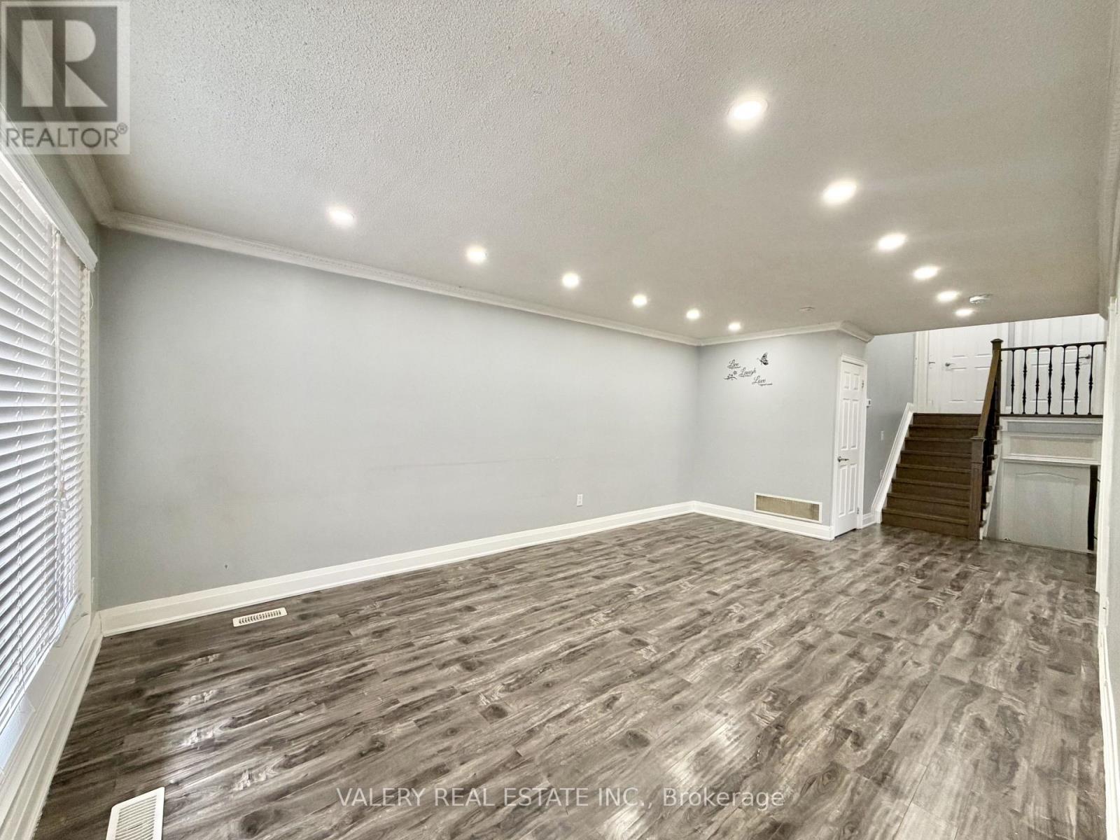A spacious room with wooden flooring and a staircase on the right side.