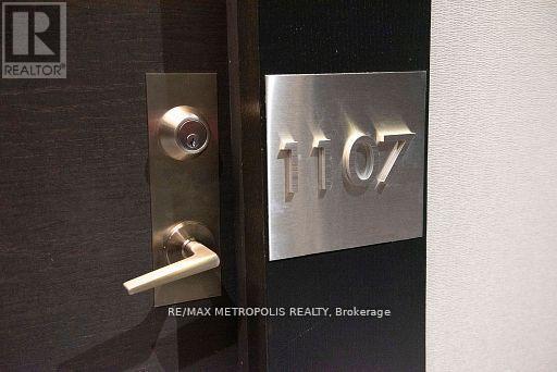 A door handle is on the left of a door with a metal plate on the right that says 1107.
