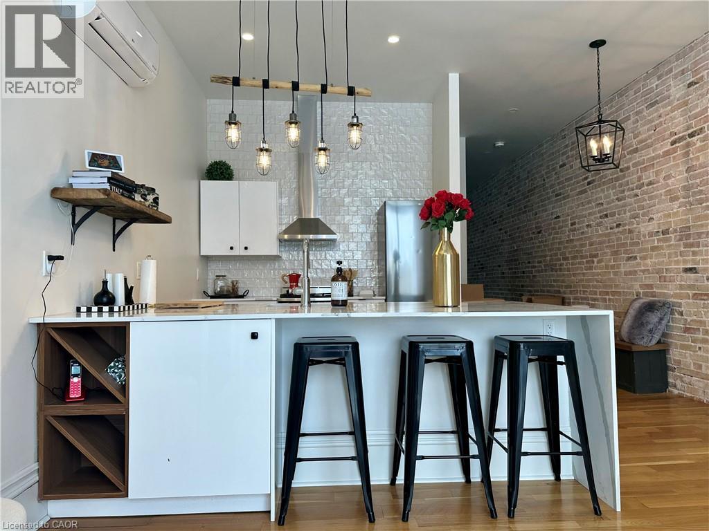 A well-lit kitchen with a bar area featuring a white countertop, bar stools, and a brick wall.