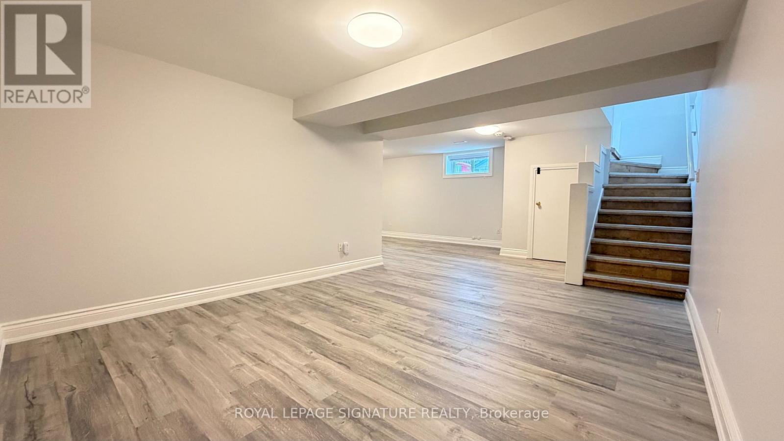 A spacious room with wooden flooring and a staircase leading to another room.