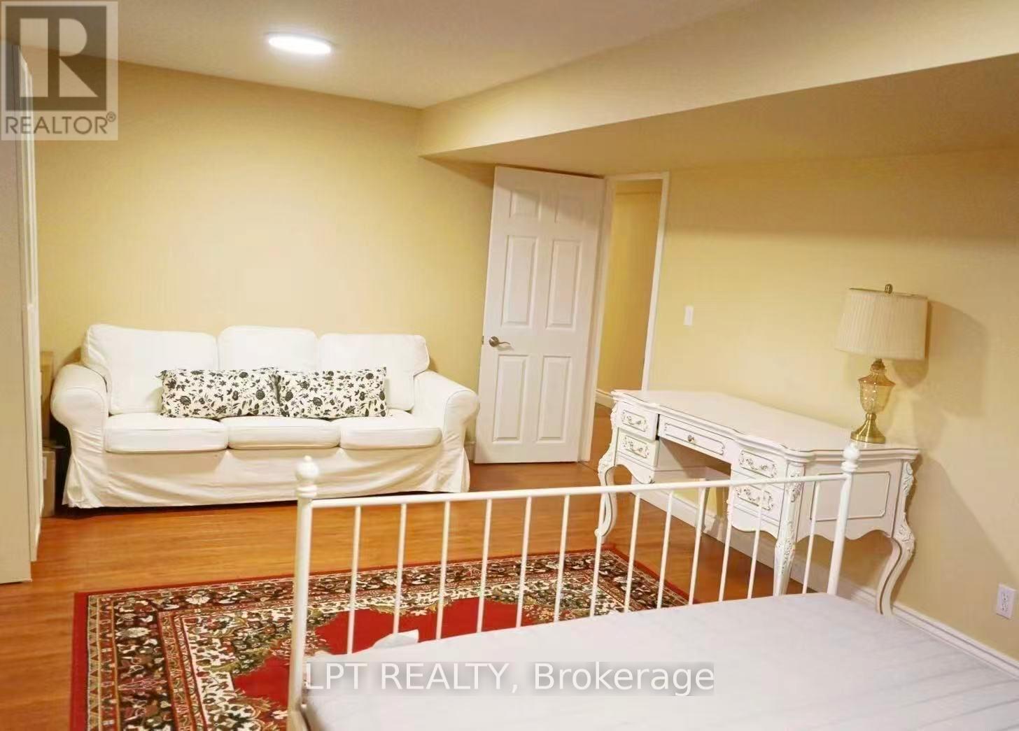A white couch with pillows sits in a room with a white desk and a white bed.