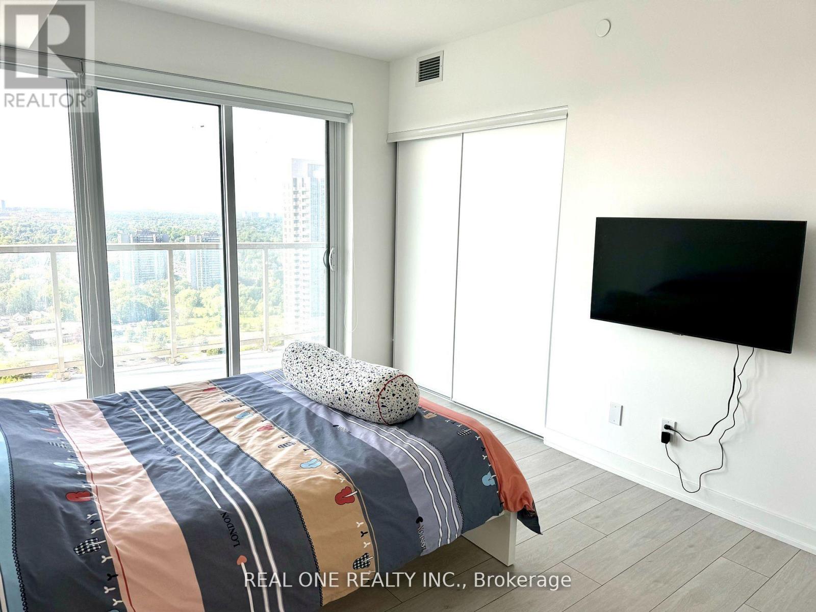 A bedroom with a bed, a television, and a window overlooking a cityscape.