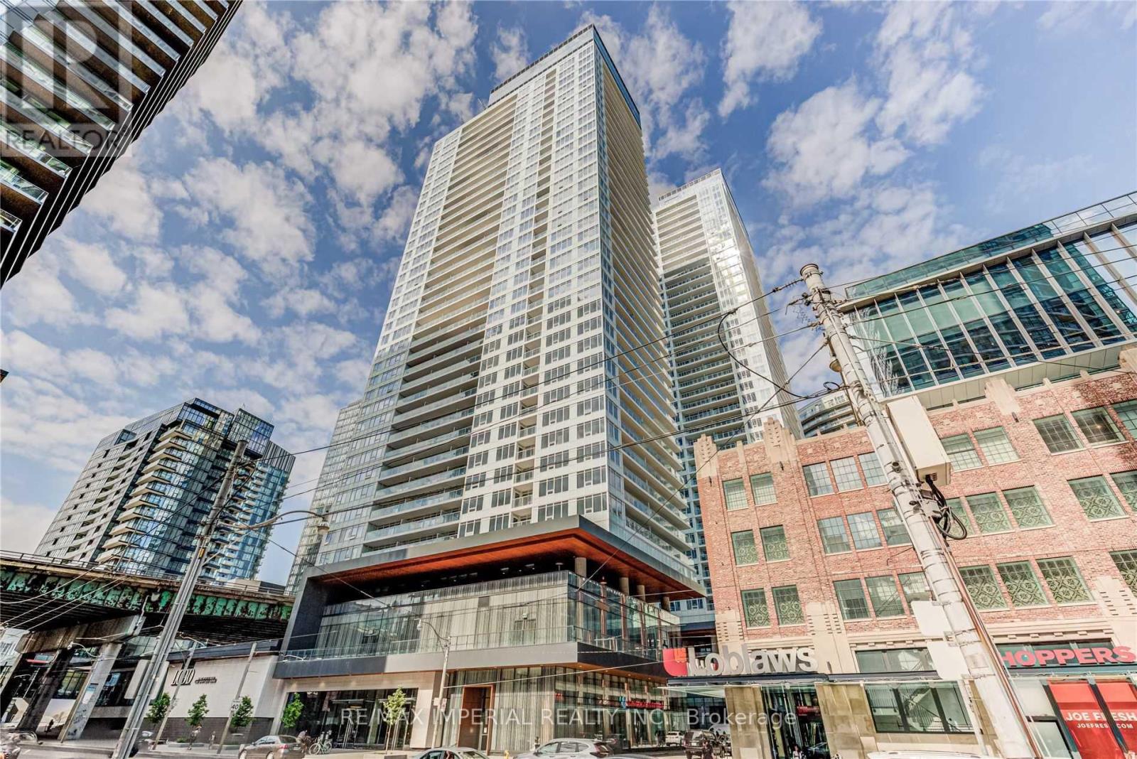 A tall building with a glass facade stands in front of a row of smaller buildings.