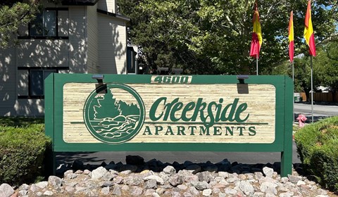 A sign for Creekside Apartments is displayed in front of a building.