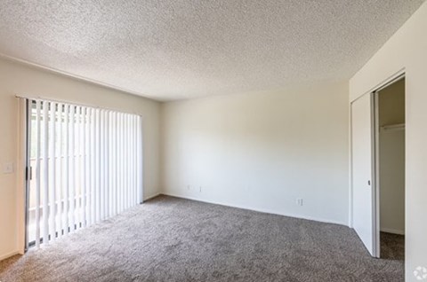 A room with a carpeted floor and a window with blinds.