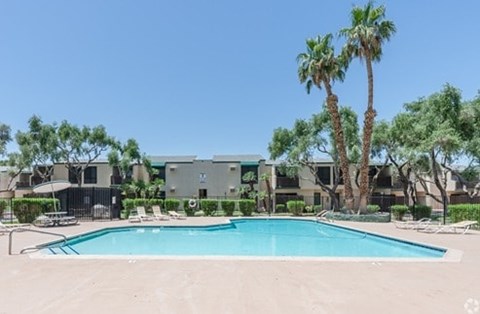 A swimming pool surrounded by palm trees and a building in the background.